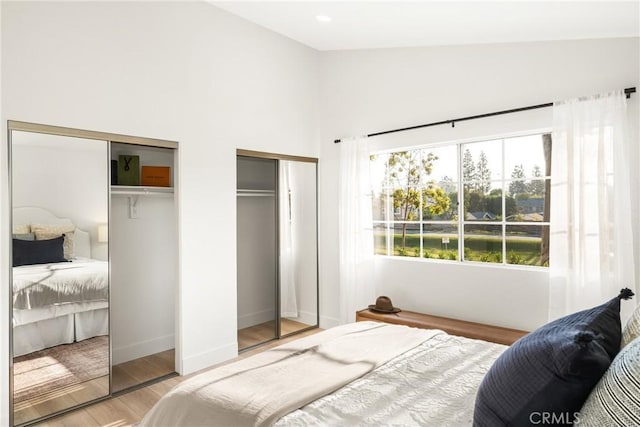 bedroom featuring lofted ceiling, wood finished floors, two closets, and baseboards