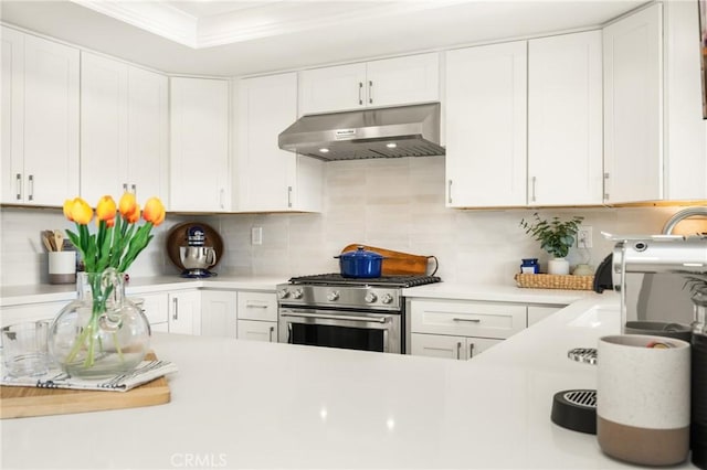 kitchen with stainless steel gas range oven, ornamental molding, light countertops, under cabinet range hood, and white cabinetry