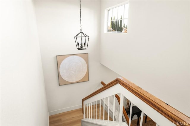 stairway with an inviting chandelier, baseboards, and wood finished floors