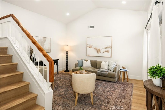 living area featuring visible vents, baseboards, stairs, vaulted ceiling, and light wood-style floors