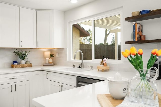 kitchen with a sink, white cabinetry, light countertops, stainless steel dishwasher, and backsplash