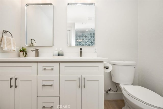 bathroom featuring double vanity, wood finished floors, a sink, and toilet