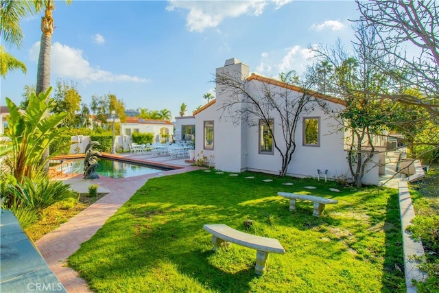 rear view of property with a lawn, stucco siding, a chimney, an outdoor pool, and a patio