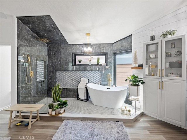 bathroom with a notable chandelier, wood finished floors, tile walls, a soaking tub, and walk in shower