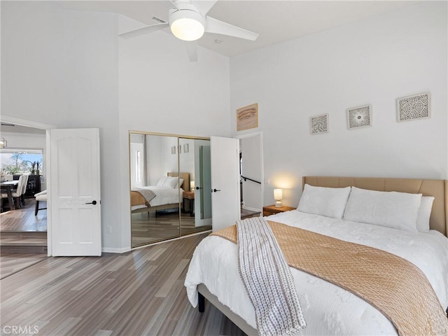 bedroom with wood finished floors, a towering ceiling, baseboards, a ceiling fan, and a closet