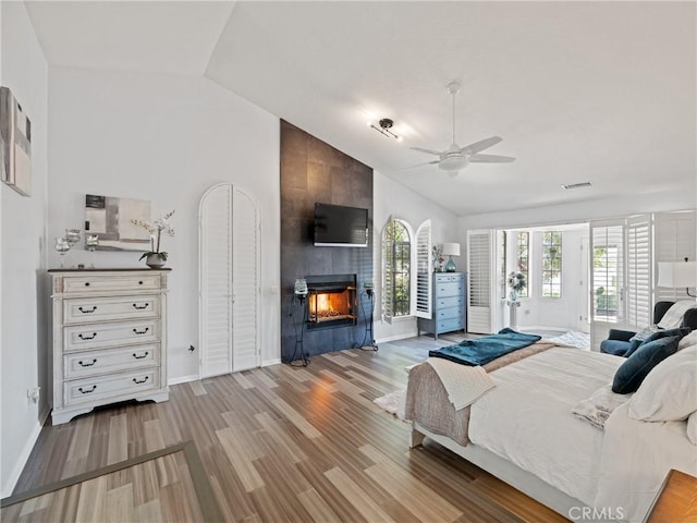 bedroom featuring access to exterior, visible vents, light wood-style flooring, a tiled fireplace, and baseboards