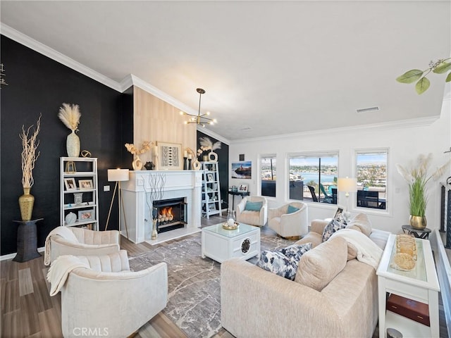 living area featuring a warm lit fireplace, an accent wall, ornamental molding, and wood finished floors