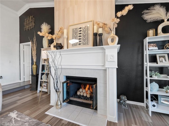 interior details with baseboards, crown molding, a tiled fireplace, and wood finished floors