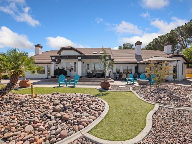 rear view of house with a tile roof, a patio, a chimney, and a lawn