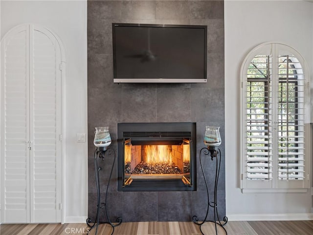 details featuring a tile fireplace, baseboards, and wood finished floors