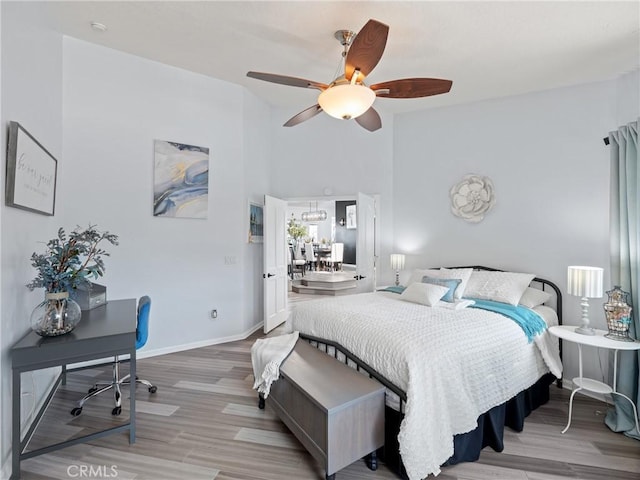 bedroom featuring ceiling fan, light wood finished floors, a high ceiling, and baseboards