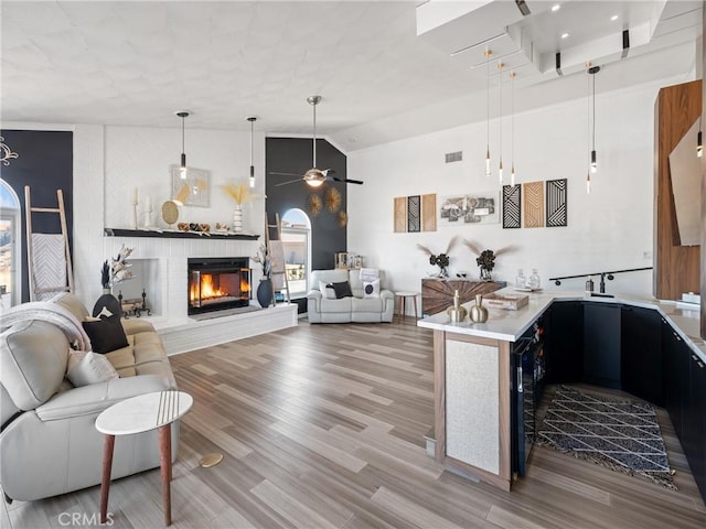 kitchen with ceiling fan, wood finished floors, open floor plan, light countertops, and a glass covered fireplace