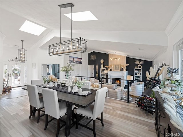 dining area featuring lofted ceiling, a warm lit fireplace, ornamental molding, and a chandelier