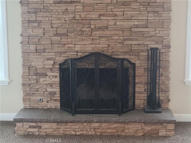 interior details with carpet floors, a stone fireplace, and baseboards