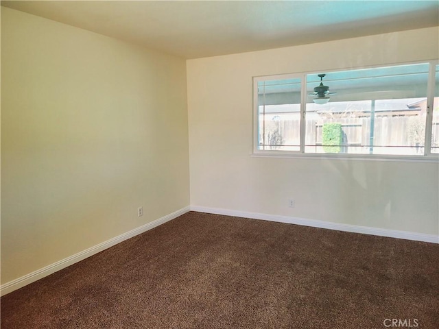 empty room featuring plenty of natural light, dark carpet, baseboards, and ceiling fan