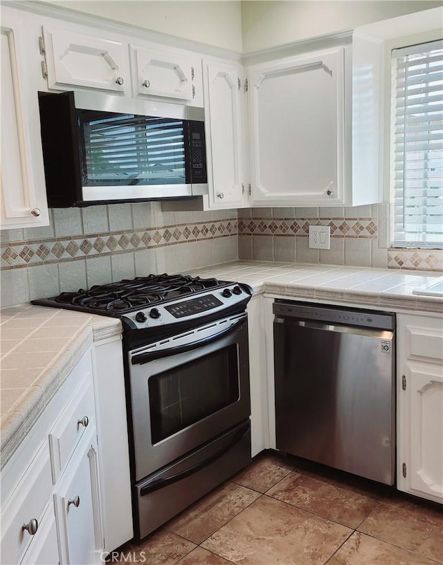 kitchen with tile countertops, white cabinets, stainless steel appliances, and decorative backsplash