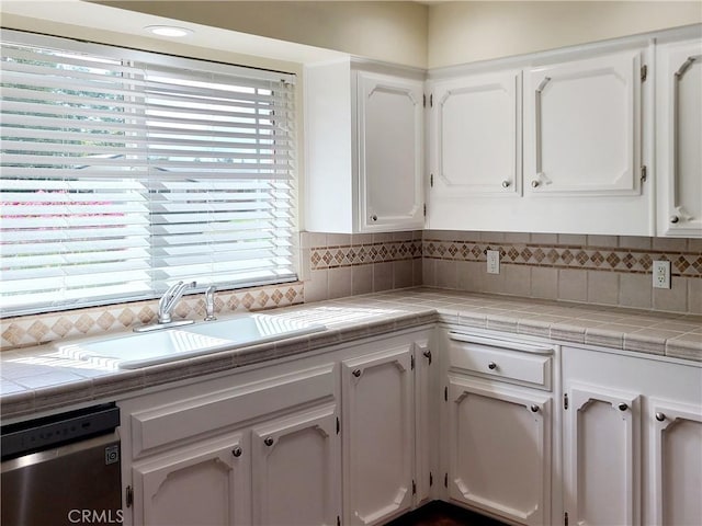 kitchen featuring tile countertops, a sink, white cabinetry, decorative backsplash, and dishwasher