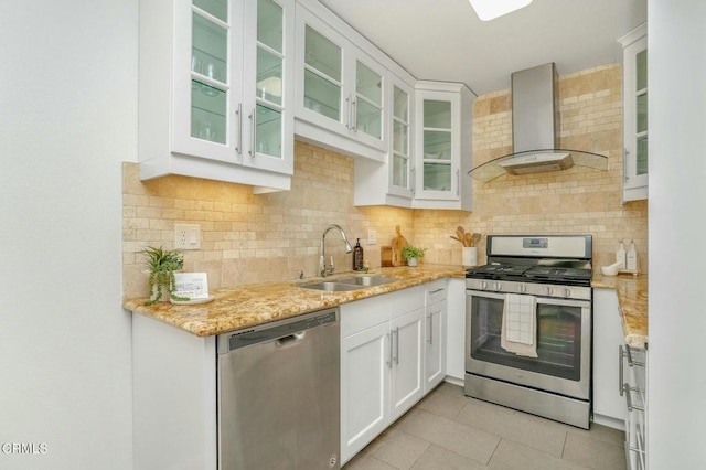 kitchen with appliances with stainless steel finishes, sink, white cabinets, light stone countertops, and wall chimney range hood