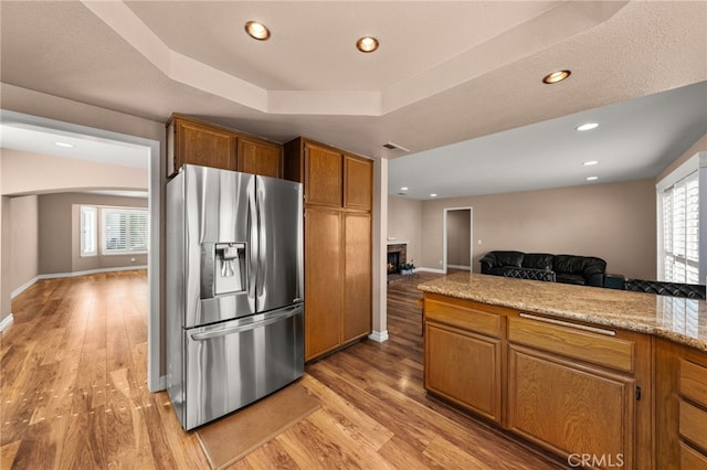 kitchen featuring plenty of natural light, light hardwood / wood-style floors, a raised ceiling, and stainless steel refrigerator with ice dispenser