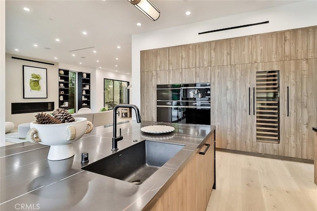 kitchen with stainless steel counters, sink, and light hardwood / wood-style floors