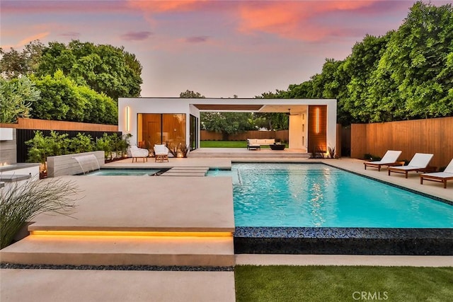 pool at dusk featuring pool water feature, an outdoor structure, and a patio