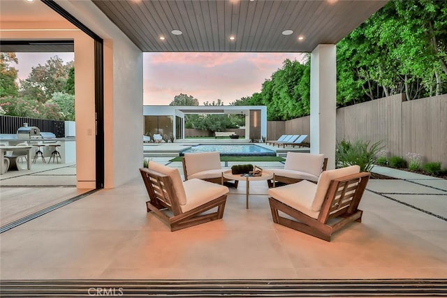 patio terrace at dusk featuring a fenced in pool, an outdoor hangout area, and an outdoor kitchen