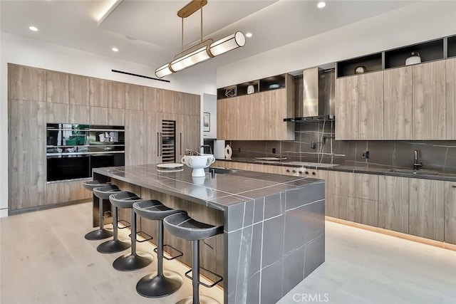 kitchen with wall chimney range hood, sink, a breakfast bar, a spacious island, and decorative backsplash