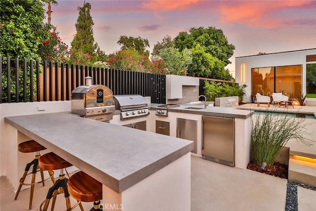 patio terrace at dusk featuring an outdoor kitchen, grilling area, and an outdoor wet bar