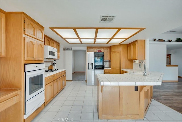 kitchen with light tile patterned floors, a peninsula, white appliances, a sink, and visible vents