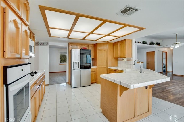 kitchen featuring light tile patterned floors, visible vents, a sink, white appliances, and a peninsula