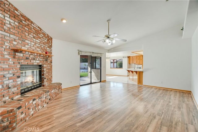 unfurnished living room featuring lofted ceiling, light wood finished floors, ceiling fan, and a fireplace