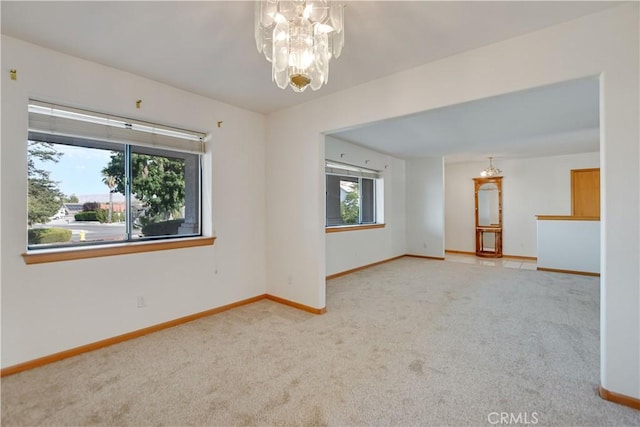 spare room featuring a chandelier, carpet, and baseboards