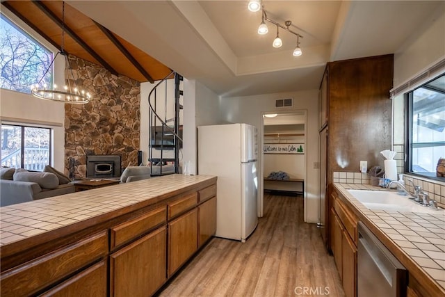 kitchen with sink, tile countertops, light wood-type flooring, white refrigerator, and stainless steel dishwasher