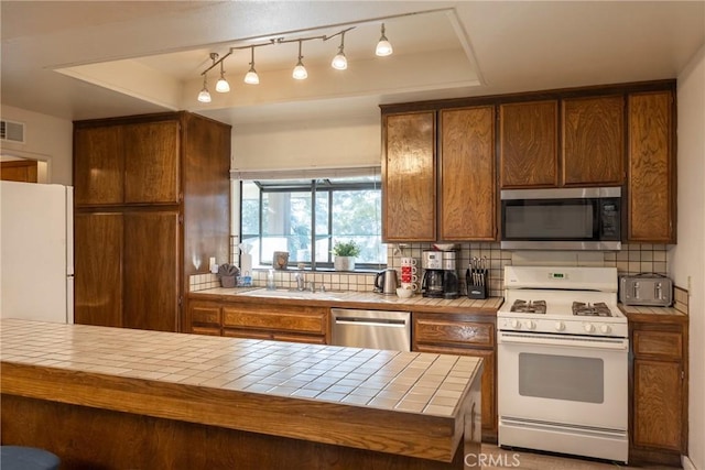 kitchen with sink, a tray ceiling, tile countertops, and appliances with stainless steel finishes