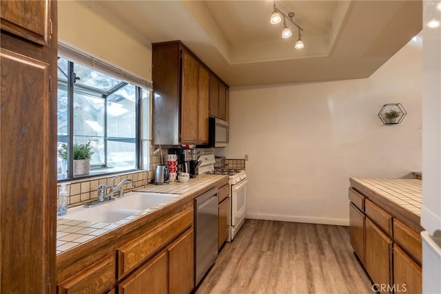 kitchen with sink, stainless steel appliances, tile counters, decorative backsplash, and a raised ceiling