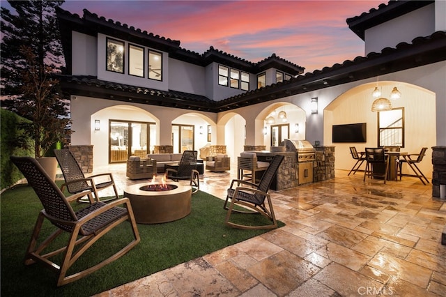 patio terrace at dusk featuring area for grilling, an outdoor living space with a fire pit, and grilling area