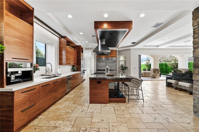 kitchen featuring sink, a breakfast bar area, a large island with sink, stainless steel built in fridge, and exhaust hood