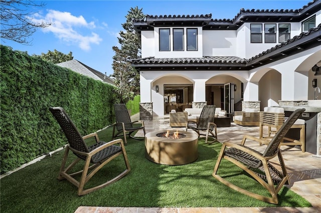 rear view of property featuring a yard, a patio, and an outdoor living space with a fire pit