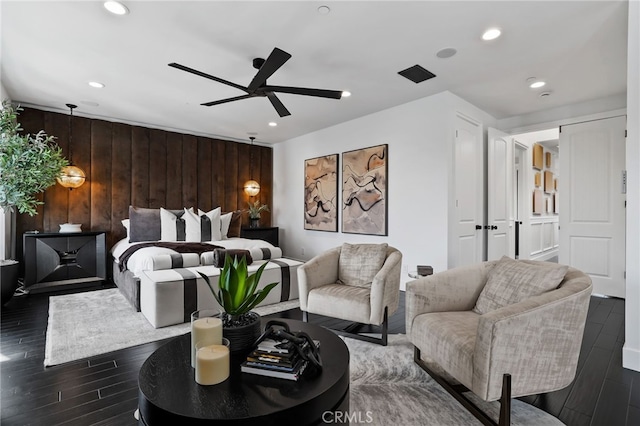 living room featuring dark wood-type flooring, ceiling fan, and wooden walls