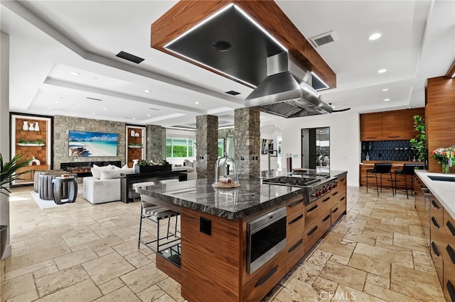 kitchen featuring ornate columns, backsplash, a large island, a tray ceiling, and stainless steel appliances