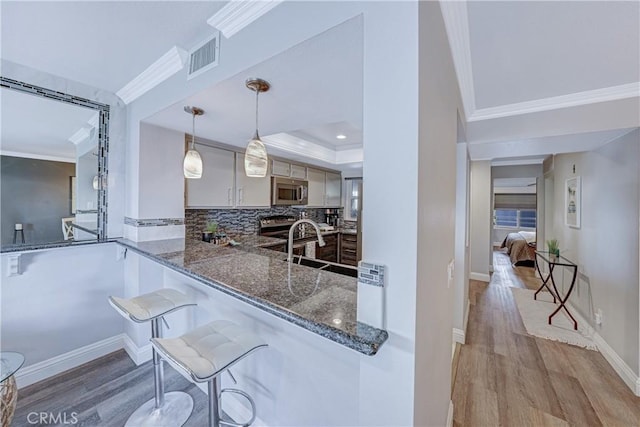 kitchen featuring a breakfast bar area, decorative light fixtures, ornamental molding, appliances with stainless steel finishes, and dark stone counters