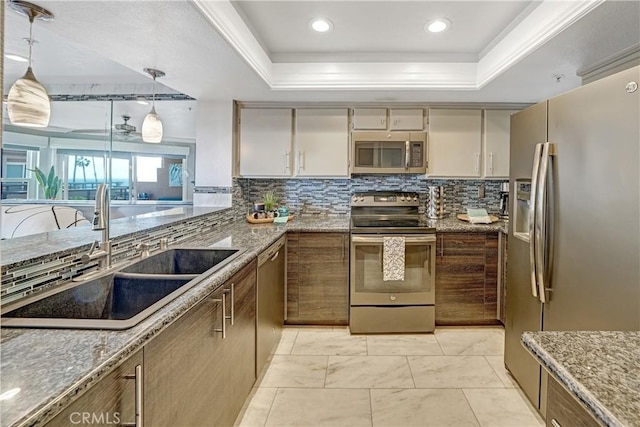 kitchen with appliances with stainless steel finishes, sink, backsplash, hanging light fixtures, and a raised ceiling