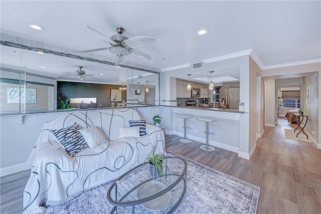 living room with ceiling fan, ornamental molding, sink, and light wood-type flooring