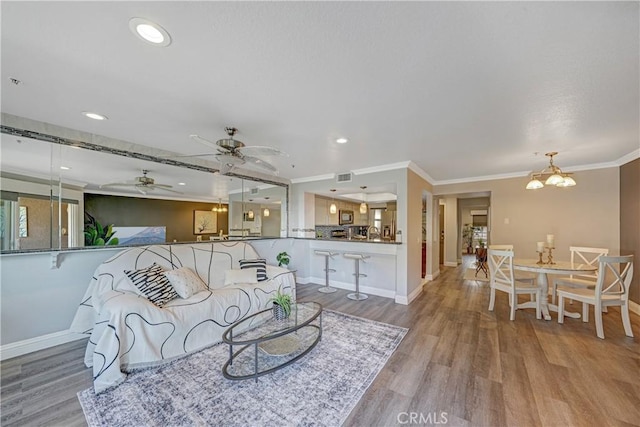 living room with ceiling fan with notable chandelier, ornamental molding, and light hardwood / wood-style floors