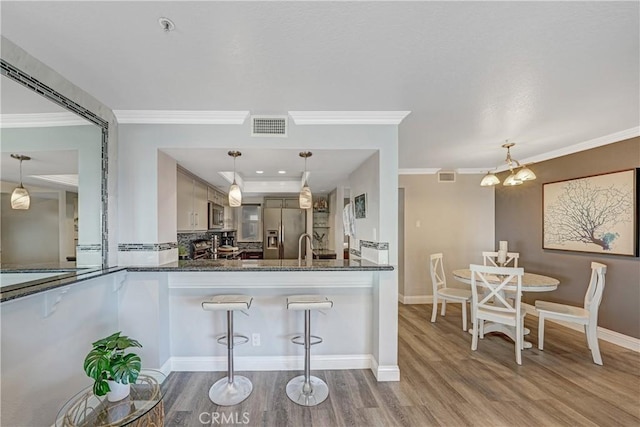 kitchen with decorative light fixtures, kitchen peninsula, dark stone counters, and appliances with stainless steel finishes