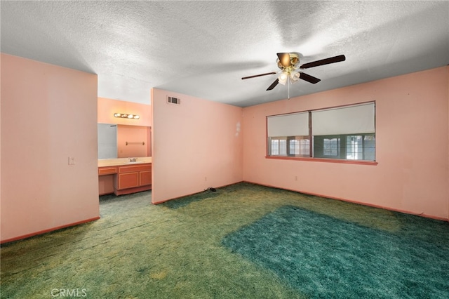 spare room with carpet floors, built in desk, visible vents, a sink, and a textured ceiling