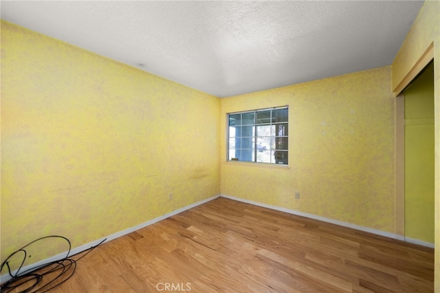 spare room with a textured ceiling, baseboards, and wood finished floors