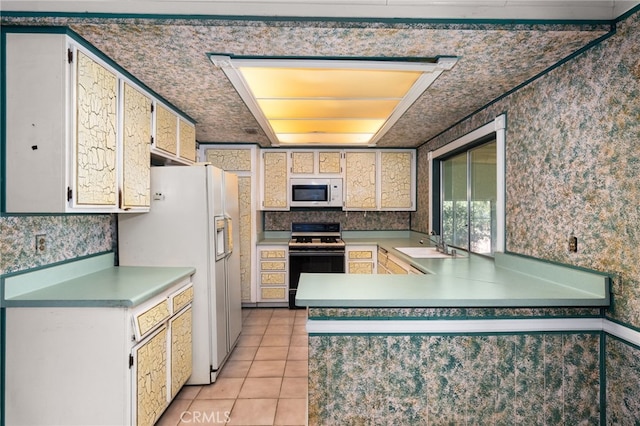 kitchen featuring a peninsula, white appliances, a sink, white cabinets, and wallpapered walls