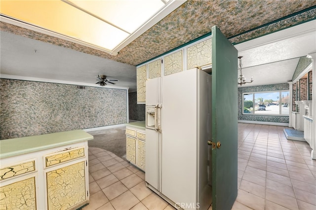 kitchen featuring wallpapered walls, white refrigerator with ice dispenser, light tile patterned flooring, light countertops, and ceiling fan with notable chandelier