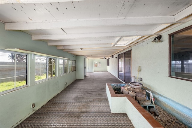 corridor with dark colored carpet and beamed ceiling